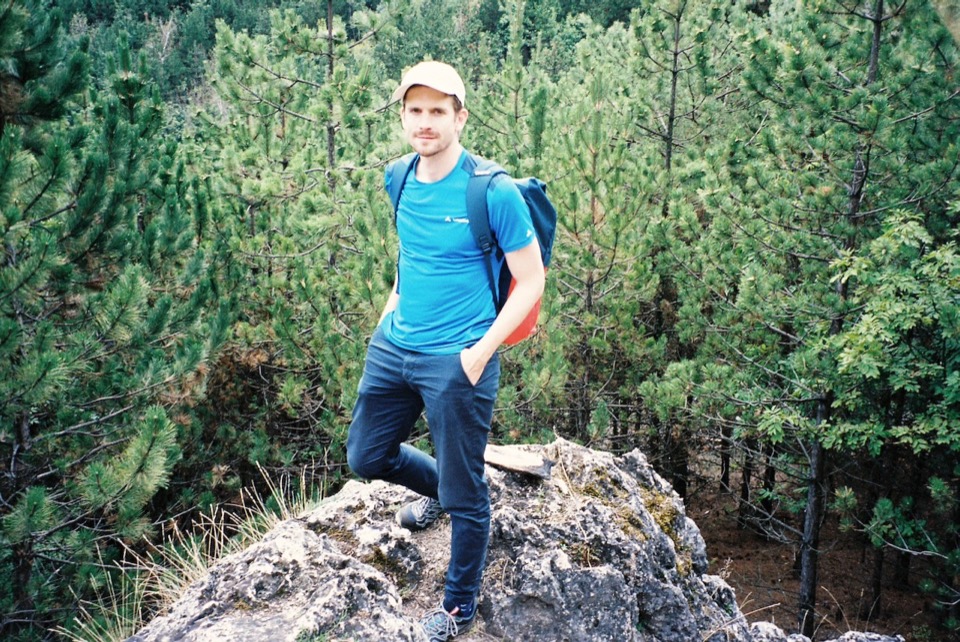 Viktor standing on a rock above a pine forest